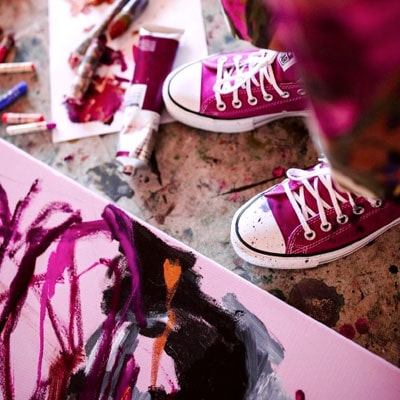 Skye's pink converse sneakers amidst paints brushes and canvases